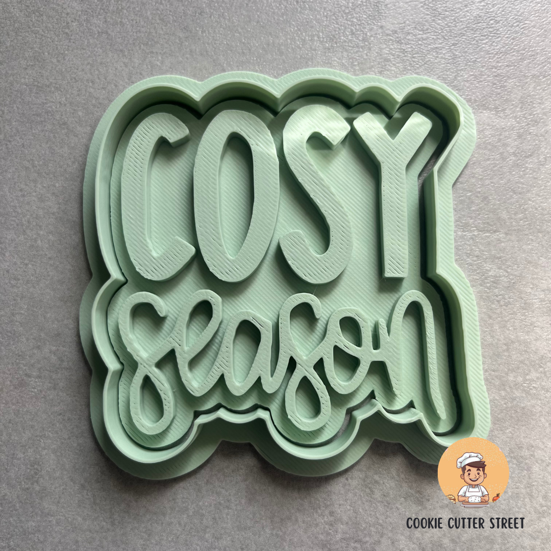 Green cookie cutter with 'COSY season' text on a gray background