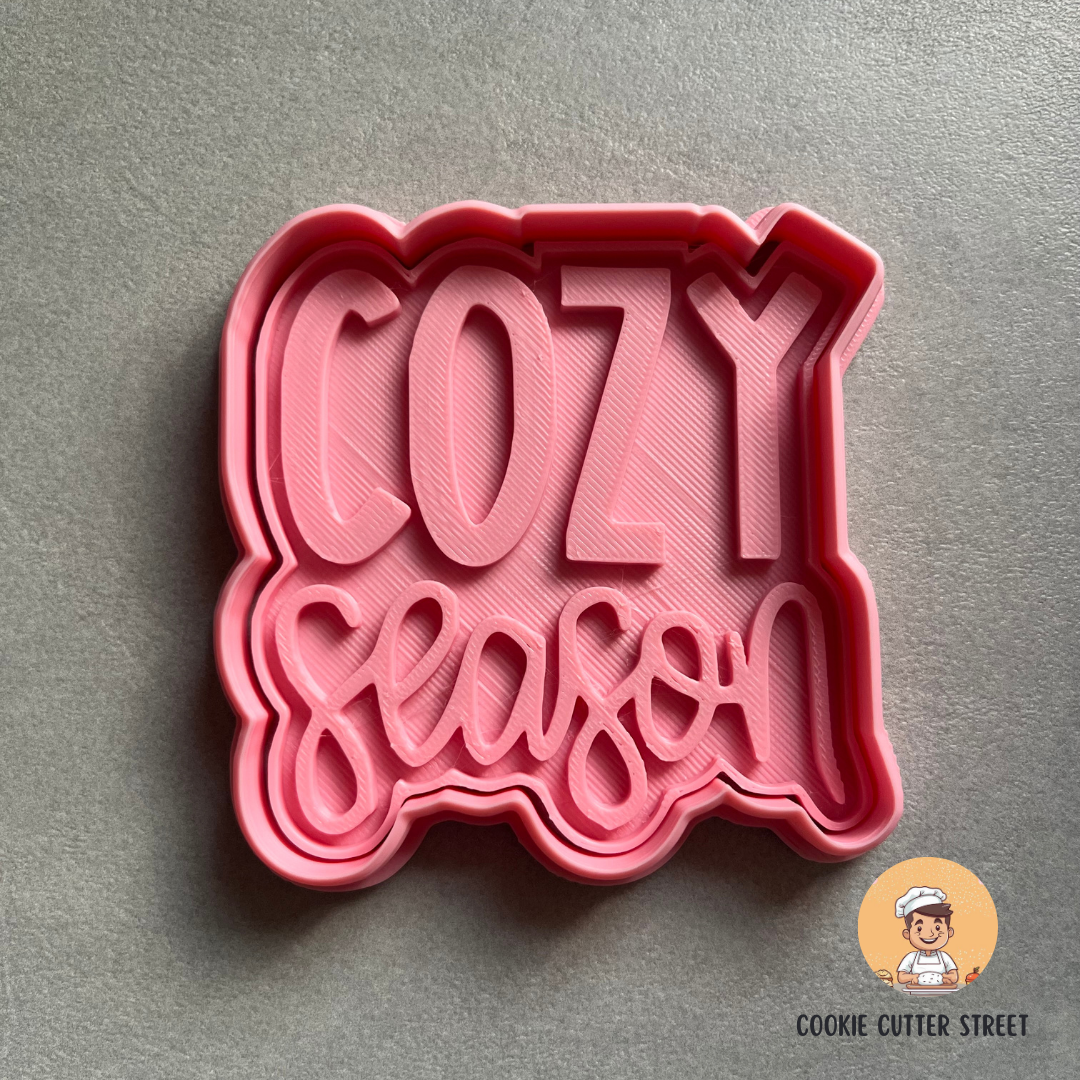 Pink cookie cutter with 'Cozy Season' text on a gray background