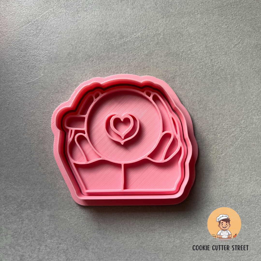 pink hands holding latte cup cookie cutter with a grey background with 'Cookie Cutter Street' logo.