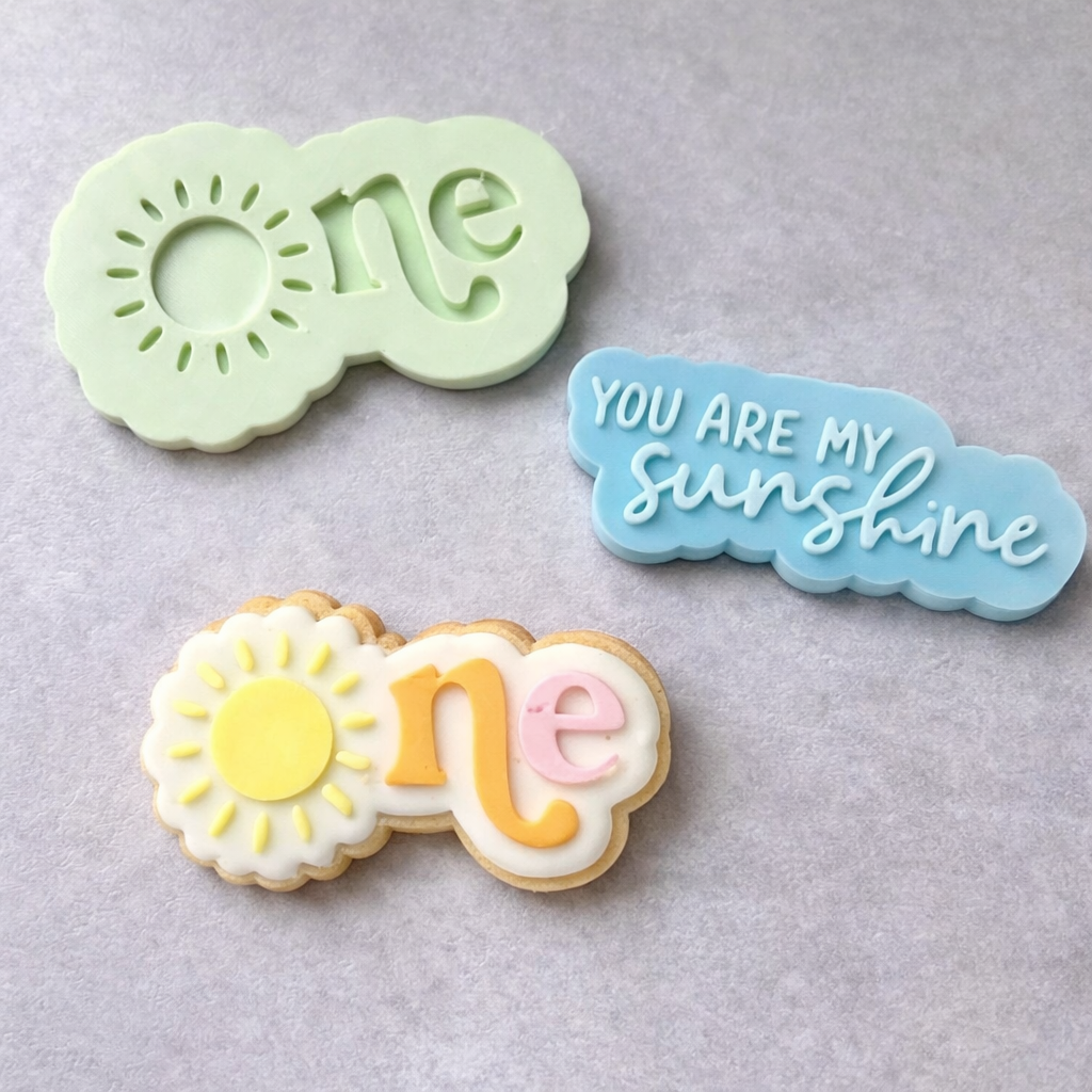 Decorative cookie cutters with 'one' and 'You Are My Sunshine' text on a gray background