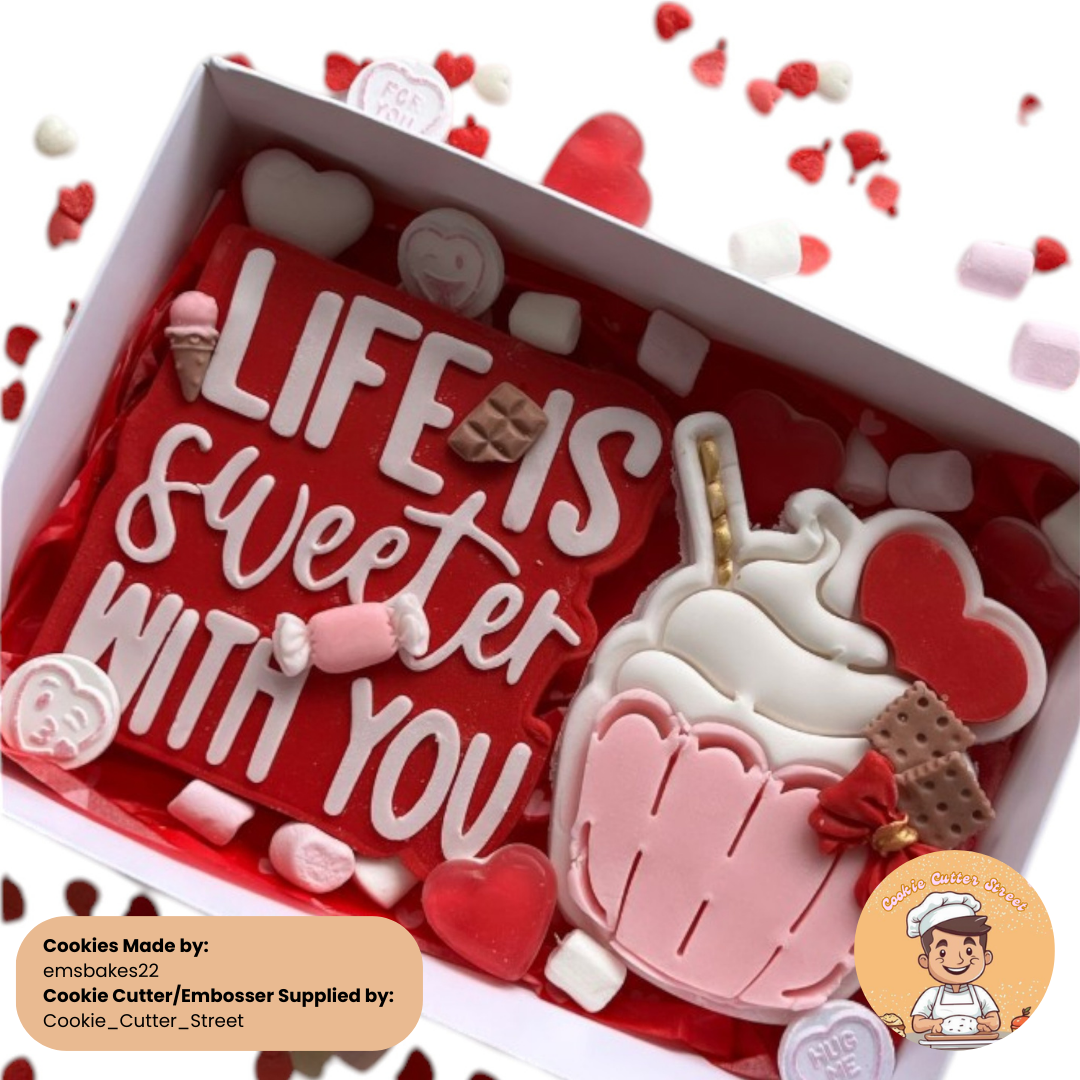 A delightful Valentine’s-themed cookie gift box showcasing a large red cookie with the phrase "Life Is Sweeter With You," paired with a pink cupcake cookie, mini candy-shaped cookies, and decorative marshmallows and hearts