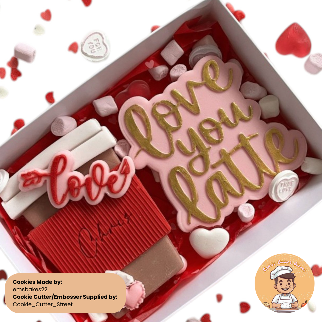 A charming Valentine’s-themed cookie gift box featuring a pink and gold cookie with the phrase "Love You Latte," a coffee cup cookie with a red sleeve, a "Love" arrow cookie, and decorative marshmallows and candies for added flair