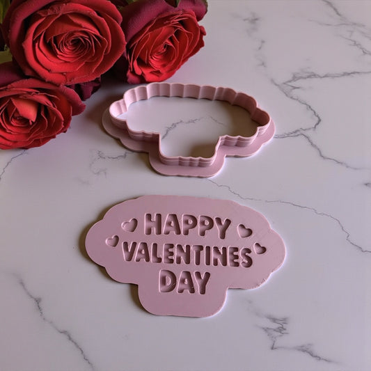 Pink 'Happy Valentine's Day' cookie cutter on a marble surface with red roses.